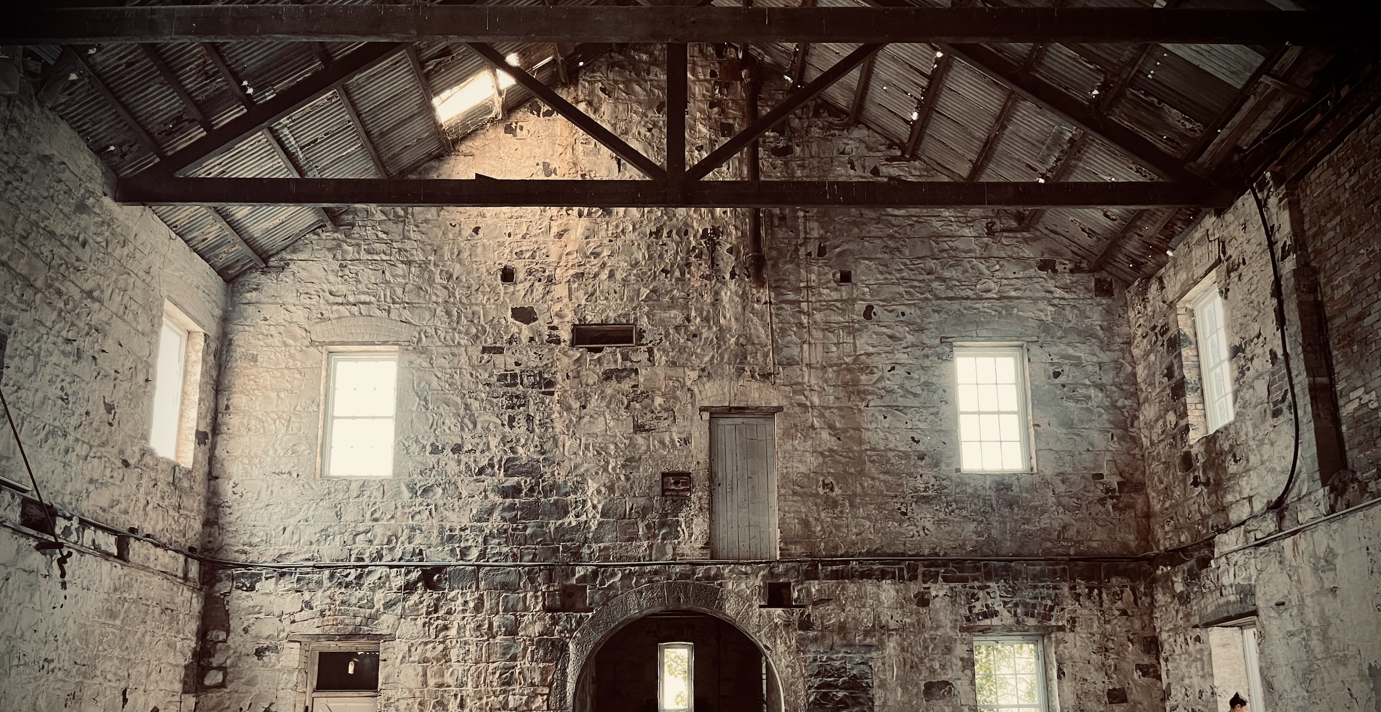 Large blue stone brick warehouse within the famous Fyansford Paper Mills in Geelong, multi colour bricks fill the wall with an archway leading to the next section at the bottom, old timber trusses in the roof holding up the rusted corrugated iron roof, this old building is being brought back to its former glory by the team at Hamilton Property Group